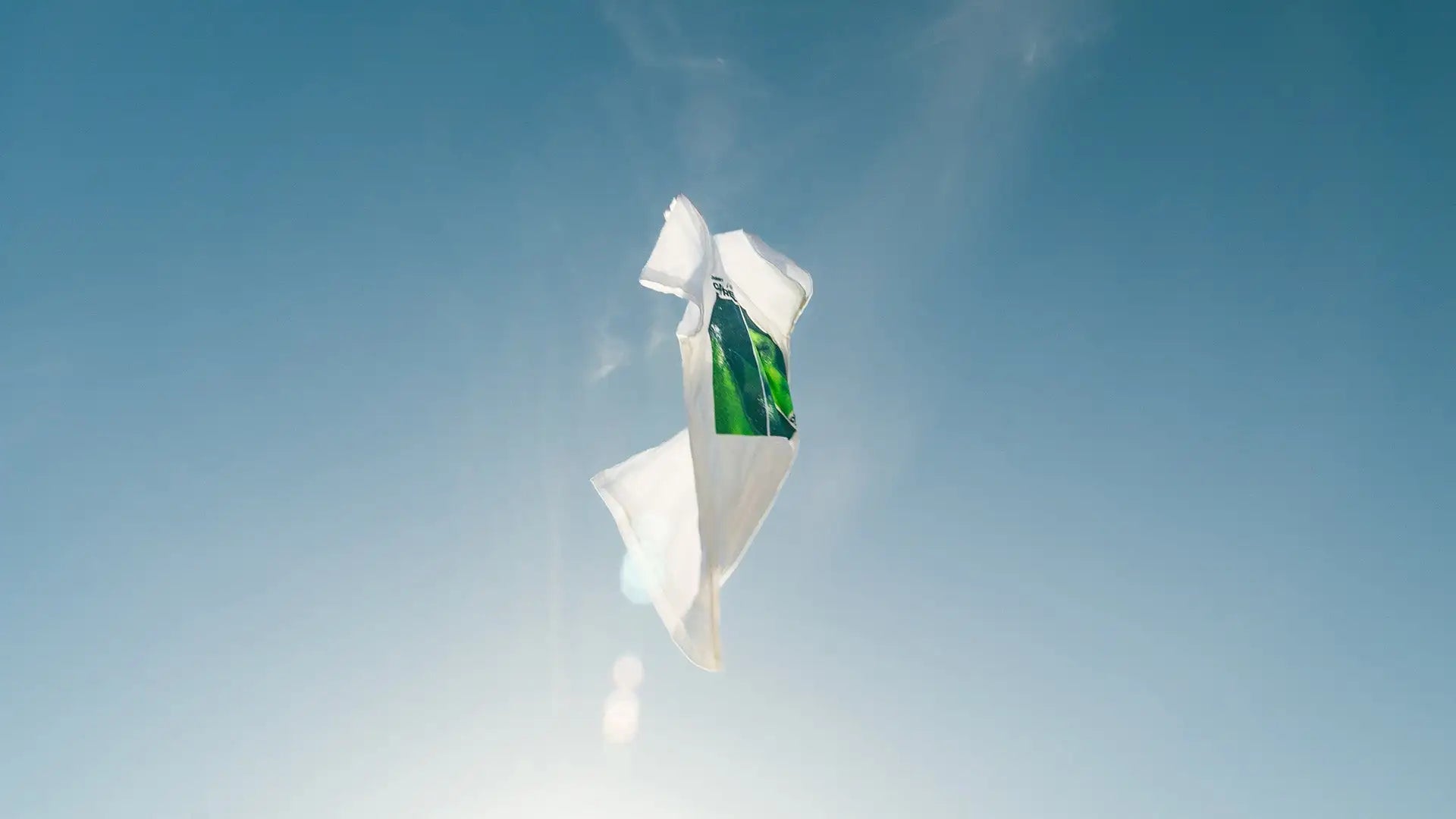 A crumpled white plastic bag with a green label floating against the sky.